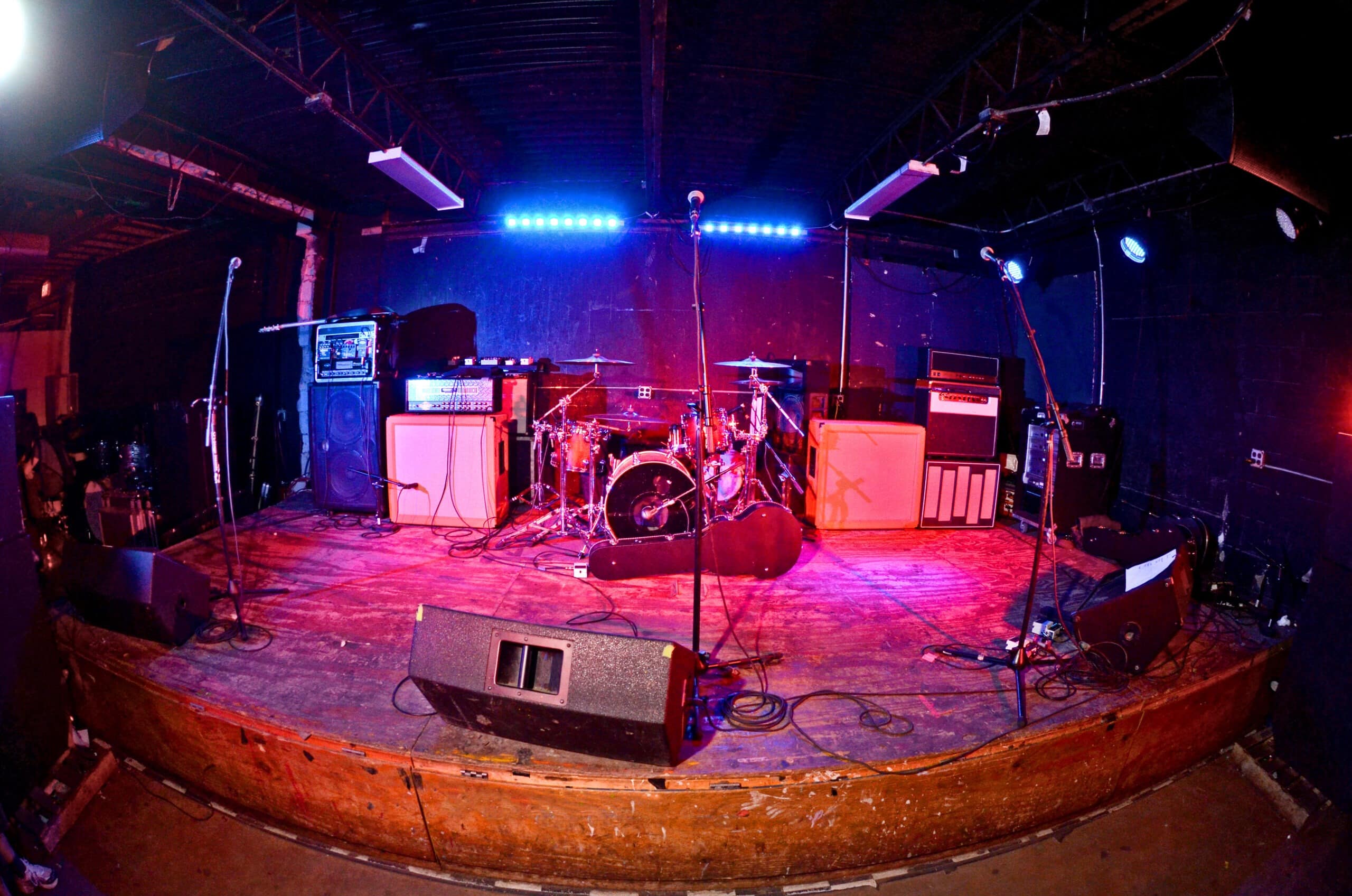 Image of a low to the ground stage with amps in the back and pink and blue lighting.