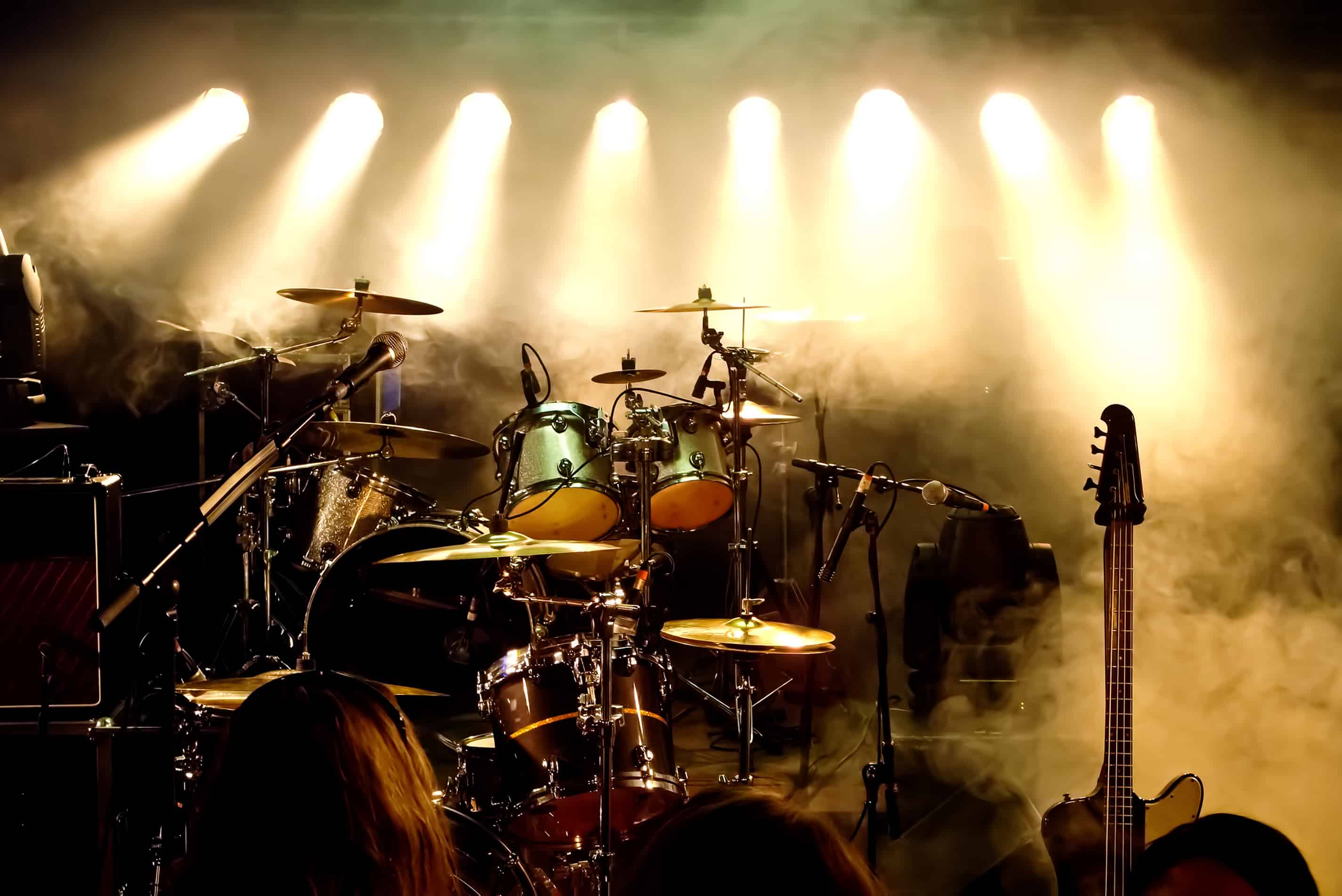 An image of a band setup with a drum set and a guitar with yellow backlighting for battle of the bands.